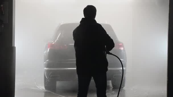 Πλύσιμο αυτοκινήτων και λεπτομέρειες. Επαγγελματίας εργαζόμενος πλένει ένα μαύρο αυτοκίνητο με πλυντήριο πίεση σε ένα πλυντήριο αυτοκινήτων. — Αρχείο Βίντεο
