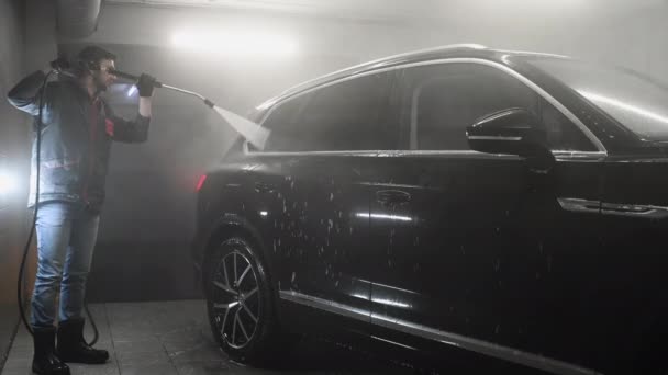 Homem lavando carro preto com jato de água de alta pressão em uma garagem. Cuidados para um automóvel. — Vídeo de Stock