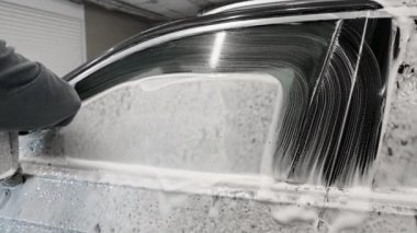 Siyah eldivenli erkek eli siyah bir arabanın yan camını ve yan aynasını yıkar..