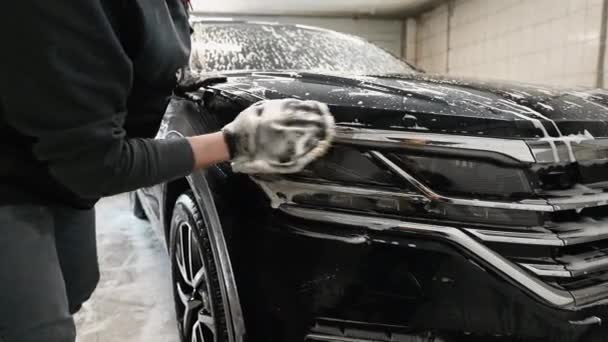 Detallado del coche - el hombre lava los faros de un coche con una mano cubierta con un guante de lavado especial, primer plano. — Vídeo de stock