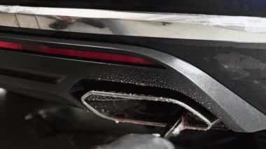 Tamirci arabanın egzoz borusunu temizliyor. Araba egzozunu köpük ve fırçayla temizliyorum. Oto yıkama..