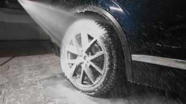 Çalışan araba yıkamada çalışıyor. Tekerlekleri köpük ve suyla yıkıyorum.