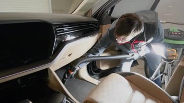 Arabanın içindeki elektrik süpürgesini kullanan adam paspaslardaki toz ve kiri temizliyor..