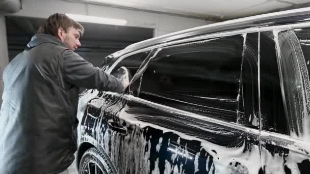 Mężczyzna pracownik w czarnej rękawicy z gąbką piankową mycie samochodu w serwisie samochodowym, myjnia samochodowa — Wideo stockowe