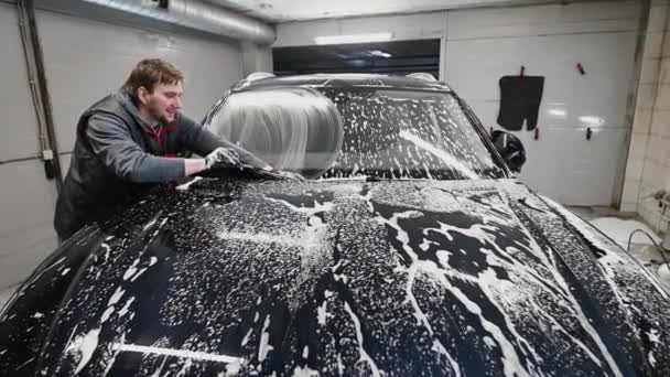 Autowaschkonzept. Mann reinigt Fahrzeug mit Putzhandschuh und Schaum, Frontscheibe. — Stockvideo