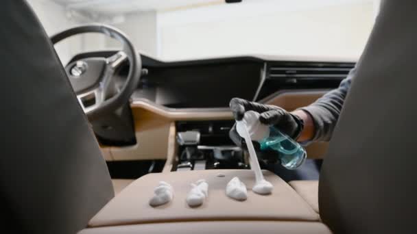 Hombre trabajador sentado dentro de un vehículo moderno, vertiendo detergente de espuma en un panel central. Detallado de coches, cuidado del cuero. — Vídeos de Stock