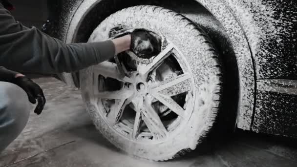 Hands of young man holding special cleaning glove, washing car wheel with foam. Cleaning of modern rims of luxury car at self car wash service. — Stock Video