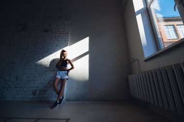 Dişi kickboksçu bir boks stüdyosunda dururken toz parçacıkları parlak arka planda uçuyor..