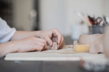 Zanaatkar elleri işlenmemiş çamurdan yapılmış kil parçalarını birbirine bağlar, usta parmaklar kil parçalarıyla çalışır, dişi ise masanın arkasındaki atölyede oturur.