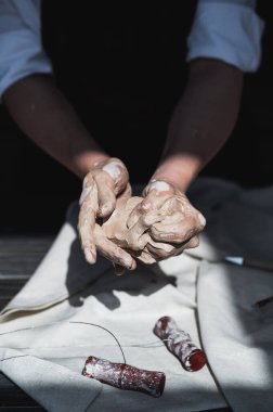 Kadın usta çömlek atölyesindeki ahşap masanın yanında kil yoğuruyor.
