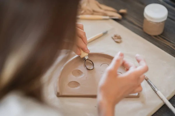 工匠的手将粘土部分与生土连接在一起，大师的手指与粘土一起工作，女性坐在桌子后面的一个车间里 — 图库照片