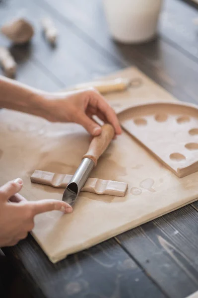 Руки майстра з'єднують глиняні частини з сирої глини, майстрині пальці працюють з шматочками глини, жінка сидить за майстернею за столом — стокове фото