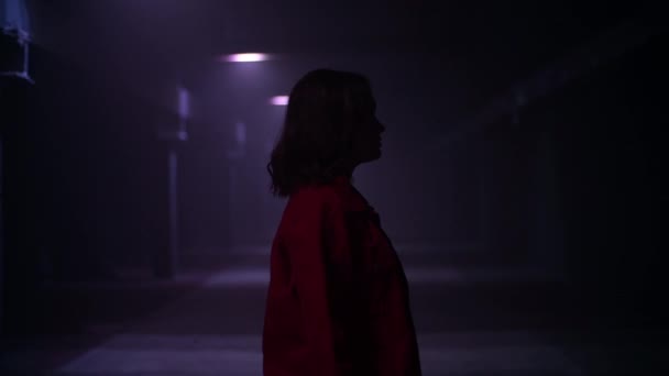 Vista lateral de una mujer de pie en un túnel oscuro con efectos de luz. Imágenes abstractas de terror de una mujer que permanece sola en la oscuridad. — Vídeos de Stock