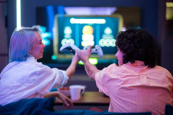 Счастливая пара играет в видеоигры дома во время самоизоляции на пандемическом карантине. Молодой человек и женщина любят проводить время вместе. Вид сзади. — стоковое фото