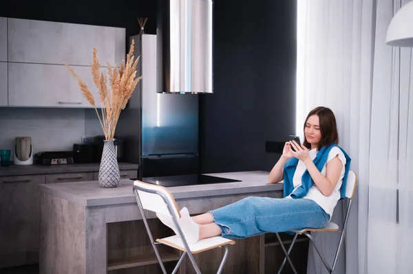 Shopping or ordering delivery online with mobile smart phone. Happy young woman using cellphone at home while sitting on a kitchen. — Stock Photo, Image