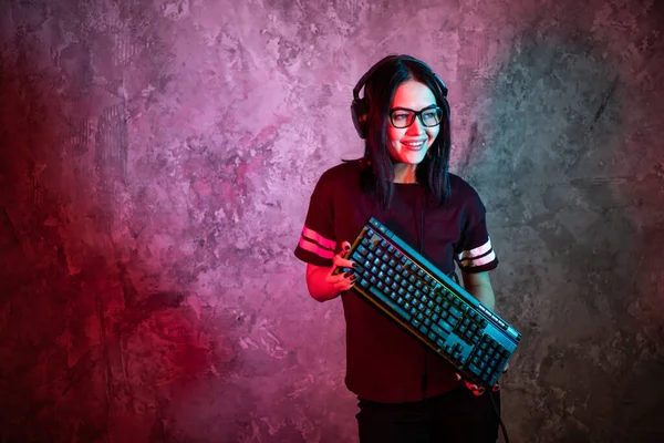 Schöne professionelle Gamer Girl mit Tastatur. Casual Cute Geek trägt eine Brille und lächelt. Cyber-E-Sport Internet-Meisterschaft. — Stockfoto