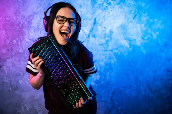Female esports gamer posing with a gaming gear in neon light. Streamer girl standing with a gaming keyboard.