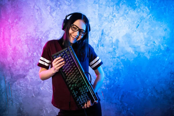 Beautiful Friendly Pro Gamer Streamer Girl Posing With the Keyboard in Her Hands, Wearing Glasses. 매력적 인게이크 소녀와 쿨 네온 리토 컬러 배경. — 스톡 사진