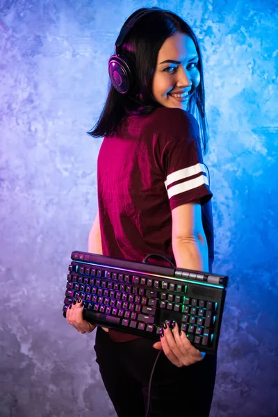 Female esports gamer posing with a gaming gear in neon light. Streamer girl standing with a gaming keyboard. — Stock Photo, Image