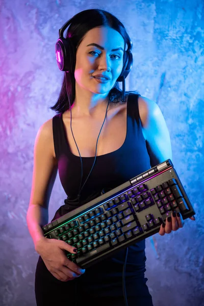 Female esports gamer posing with a gaming gear in neon light. Streamer girl standing with a gaming keyboard. — Stock Photo, Image