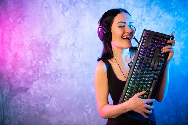 Female esports gamer posing with a gaming gear in neon light. Streamer girl standing with a gaming keyboard. — Stock Photo, Image