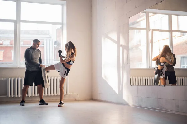 Femmina combattente arti marziali praticando con allenatore, punzonatura taekwondo calcio pad esercizio calci. Formazione di kickboxer donna colpisce con guantoni piede nudo sacco da boxe scudo calci — Foto Stock