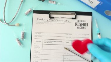 Doktor eldiveni küçük kırmızı kalbi kovid 19 aşı kartına yerleştirdi.