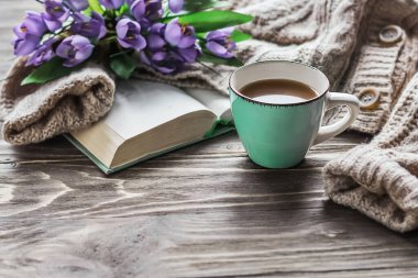  Sabah kahvesi. Tahta bir masada bir fincan kahve, açık bir kitap ve bir buket bahar çiçeğinin arka planında sıcak bir süveter. Hayat konsepti. Sıcak bir sabah.