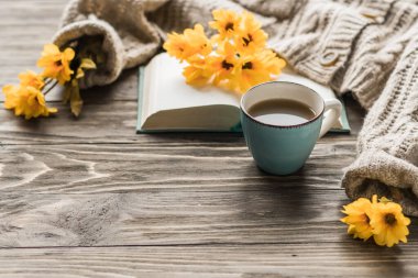 Bahar sabahı kahvesi. Tahta bir masada bir fincan kahve ve sarı çiçeklerin arka planına karşı sıcak bir süveter. Hayat konsepti. Boşluğu kopyala. 