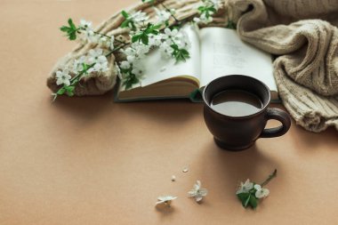 Bahar sabahı kahvesi. Bir fincan kahve, açık bir kitap ve çiçek açan dalların arka planında sıcak bir süveter. Sıcak bir sabah. Boşluğu kopyala.