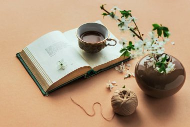 Kafenin içinde. Bir vazoda çiçek açan dallar, açık bir kitap ve bej renkli arka planda bir fincan kahve. Kafe için arka plan, metin için yeri olan reklam arkaplanı kavramı. 