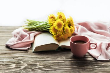Sabah kahvesi. Açık bir kitabın üzerinde bir buket sarı karahindiba ve ahşap bir masanın üzerinde bir fincan kahve. Sıcak bir sabah. Boşluğu kopyala.