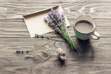 Kağıt bir zarfın üzerinde lavanta buketi ve fotokopi alanı olan ahşap bir masada bir fincan kahve..