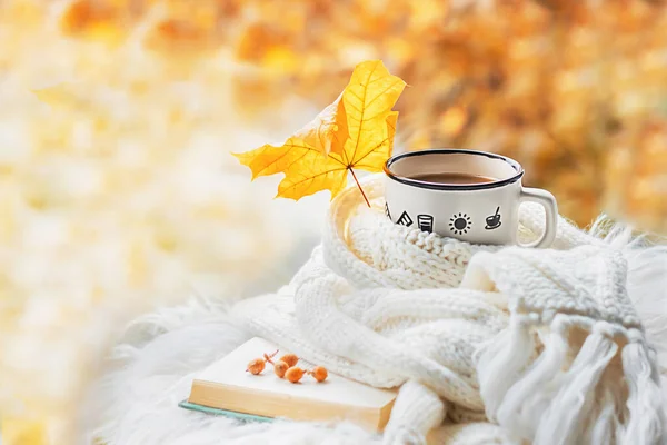 Autumn morning. A cup of coffee or hot tea on an open book and a warm sweater against a background of autumn leaves. Still life concept. Copy space.
