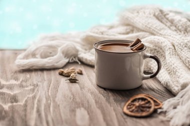 Bir kupa sıcak çikolata ya da ahşap bir masanın üzerinde tarçın çubukları olan kakao. Sıcak eşarp ve sıcak sonbahar kış konsepti. Arka planda bulanık bokeh.