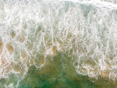Aerial view of the sea with an emerald green color and large foaming waves
