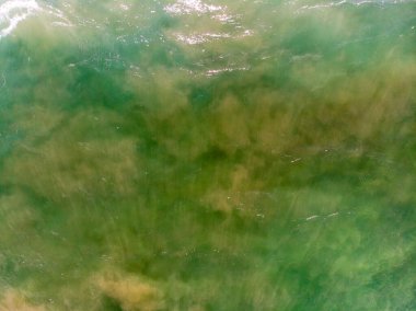 Aerial view of the sea with an emerald green color and large foaming waves