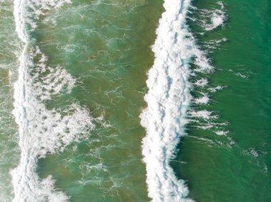 Aerial view of the sea with an emerald green color and large foaming waves