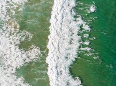 Aerial view of the sea with an emerald green color and large foaming waves
