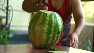 Bir adam büyük bir karpuz kesiyor.