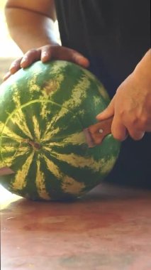 Bir adam büyük bir karpuz kesiyor.