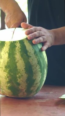 Bir adam büyük bir karpuz kesiyor.