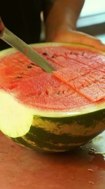 Bir adam büyük bir karpuz kesiyor.