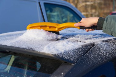 Bir fırçayla arabanın çatısından kar temizliyorum. Boşluğu kopyala.