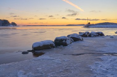 Deniz kıyıları buzla kaplı ve gün batımında kar altında. Boşluğu kopyala.
