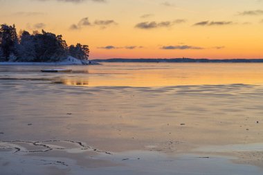 Deniz kıyıları buzla kaplı ve gün batımında kar altında. Boşluğu kopyala.