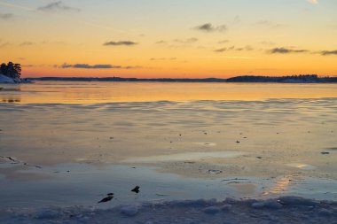 Deniz kıyıları buzla kaplı ve gün batımında kar altında. Boşluğu kopyala.