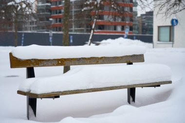 Arkasında çok katlı evler olan karların altında ahşap bir bank. Boşluğu kopyala.
