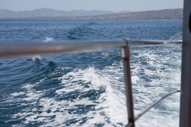 Köpüklü dalgalar arka planda kıyı sahili ile birlikte geminin güvertesinde.