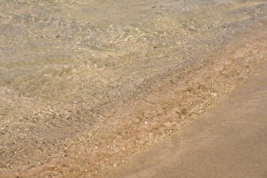 Girit 'teki tropikal kumlu sahilde berrak dalgalar ve renkli kumlar